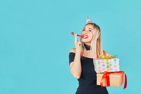 Young woman with gift box and blowing party horn or noisemaker while celebrating birthday on blue background — Stock Photo, Image