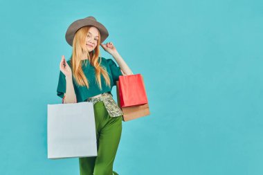 Alışveriş torbaları tutan mutlu genç kadın kalıyor. Güzel kız alışveriş merkezinde yürür, mavi arka planda bir sürü çanta taşır..