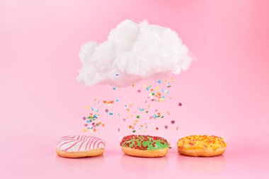 Colored sprinkles fall from cloud. Assorted donuts frosted, pink glazed and sprinkles on pink background. Various decorated doughnuts as concept of a fresh delicious Breakfast. clipart