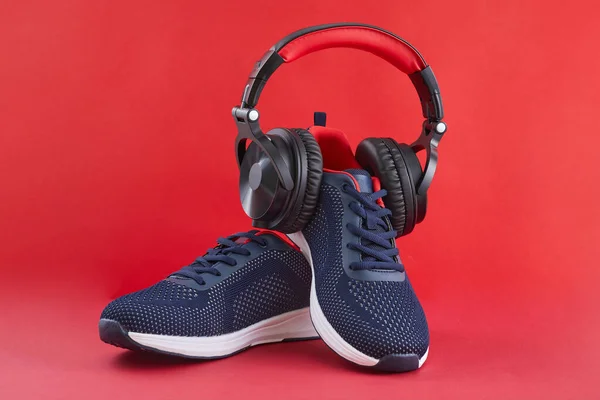 Zapatillas de deporte y auriculares azules en un fondo rojo. Concepto deportivo y musical. —  Fotos de Stock