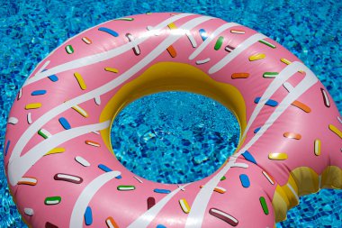 Yüzme havuzunda yüzen pembe şişirilebilir donut donutu. Plaj havuzu aksesuarları. Yaz tatili kavramı.