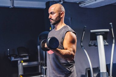 Spor salonunda dambıllarla spor yapan atletik bir genç.