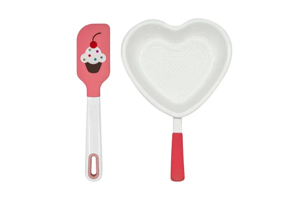 Beyaz kalp şekilli seramik pişirme kabı ve beyaz üzerine pembe spatula. — Stok fotoğraf