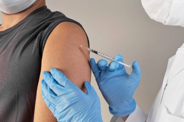 Aşı konsepti. Eldivenli doktor şırıngalı delikanlıyı aşılıyor.