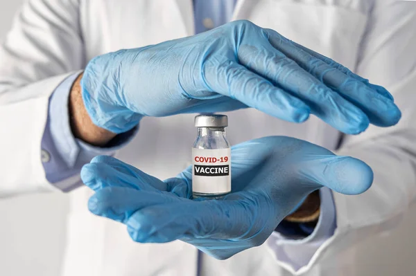Концепція вакцинації від коронавірусу в руці лікаря скляної вакцини ампула. Білий халат і рукавички — стокове фото