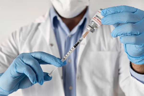 Концепція вакцинації від коронавірусу в руці лікаря скляної банки для ампули. Білий халат і рукавички — стокове фото