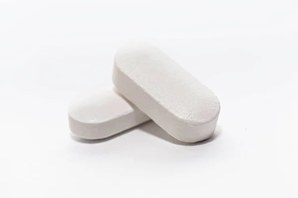 Närbild av två vita tablettkapslar på vit bakgrund — Stockfoto