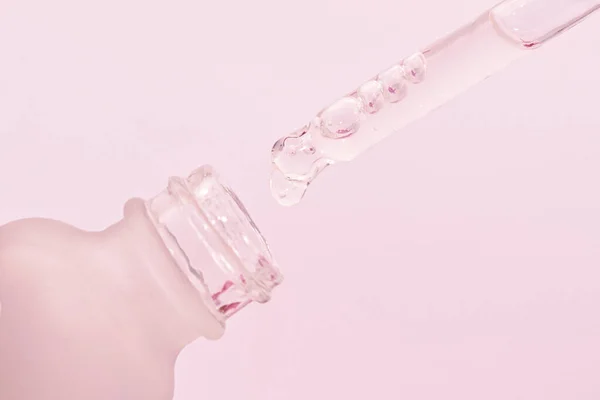 yüz serumu, cam damlası kavanozu ve pembe arka planda pipeti olan makroyu kapat.
