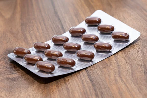Buwn medicinska kapslar piller i transparent blisterförpackning på träbord — Stockfoto