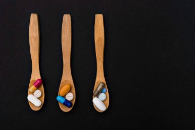 Yakın plan renkli toz yumuşak kapsüller tahta kaşıkta vitamin hapı. mavi, sarı, kahverengi, siyah arka plan.