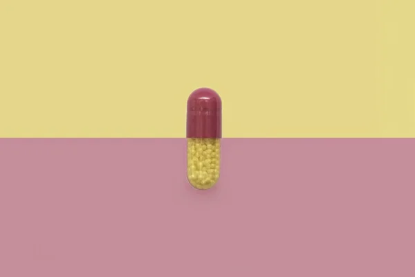 Крупним планом один барвистий порошок м'якої капсули таблетки на рожево-жовтому тлі. лікарська добавка — стокове фото