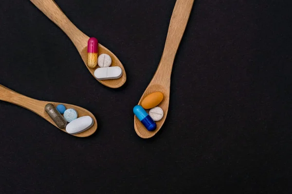 Närbild färgglada pulver mjuka kapslar piller vitamin i träsked. blå rosa gul brun tillägg svart bakgrund — Stockfoto
