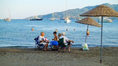 İnsanlar sahilde deniz kenarında rahatça oturuyorlar. Marmaris Türkiye Ağustos 2021             