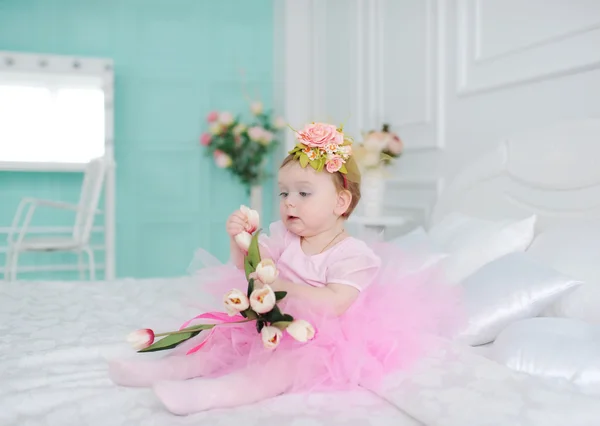 La niña con tulipanes se sienta en una cama . — Foto de Stock