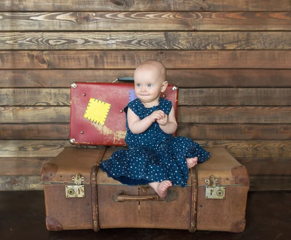 The little girl in blue dress sits on big suitcase. — Stock Photo, Image