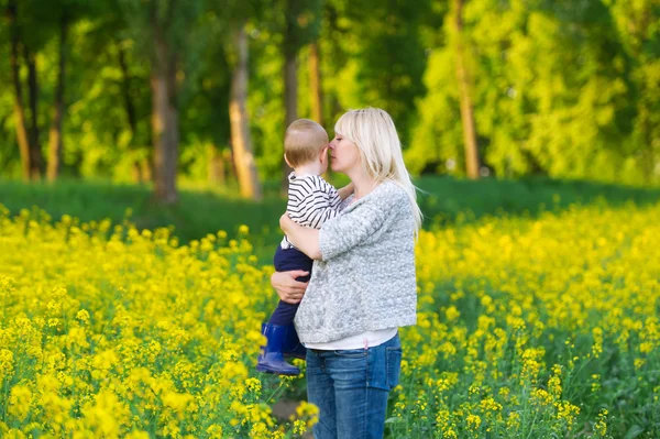 Mother with son have a rest on yellow rape field. — Stock Photo, Image