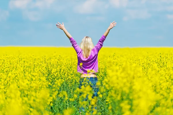 The young blonde in jeans walks on the rape field. — Stock Photo, Image