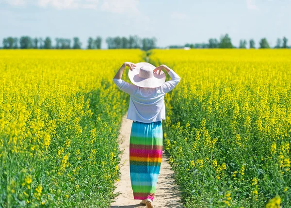 Kobieta w kapeluszu spacery na polu rzepaku. — Zdjęcie stockowe