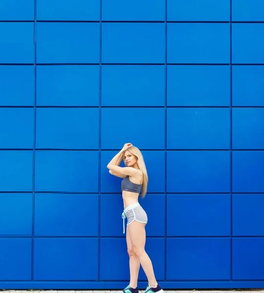 A bela esportista posa em um fundo azul . — Fotografia de Stock