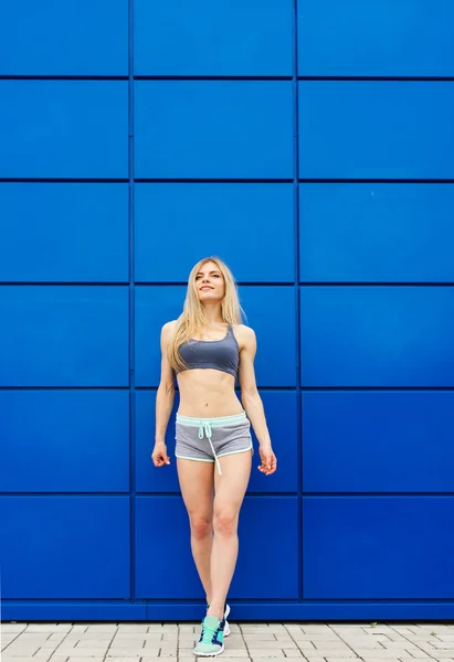 The beautiful sportswoman poses on a blue background. — Stock Photo, Image