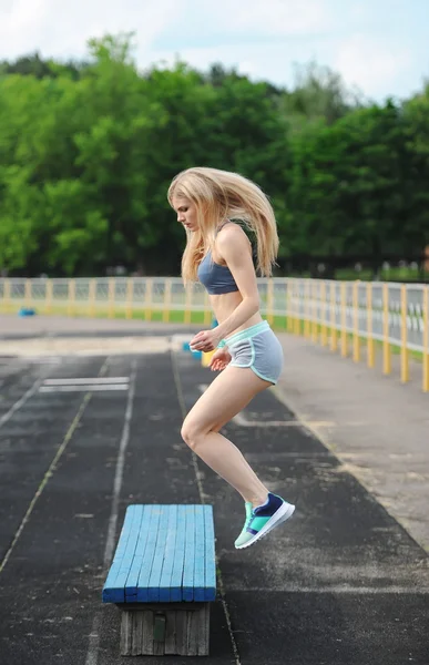 The beautiful sportswoman jumps on a bench up. — Stock Photo, Image