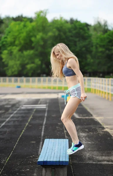The beautiful sportswoman jumps on a bench up. — Stock Photo, Image