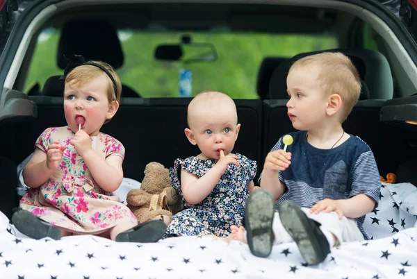 Tres niños en el portaequipajes del coche comen caramelos . — Foto de Stock