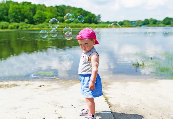 De kosten van het meisje aan oever van lake. Rond haar bubbels vliegen. — Stockfoto