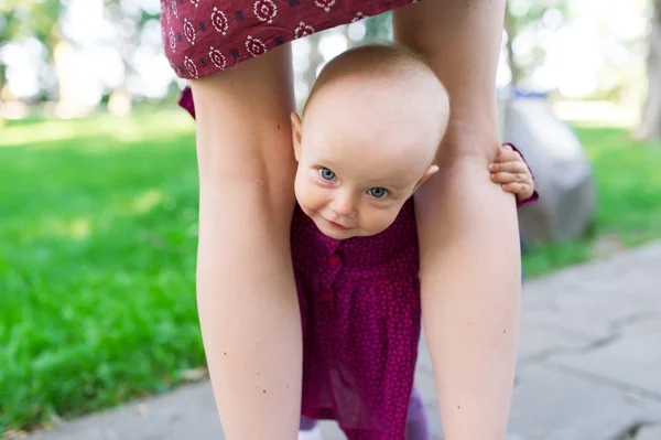 Retrato de bebé agradable sosteniendo las piernas de la madre — Foto de Stock