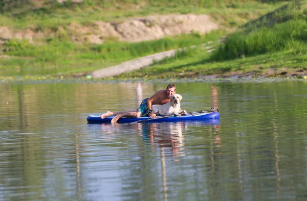 Pies i float człowieka przez łódź na jeziorze. — Zdjęcie stockowe