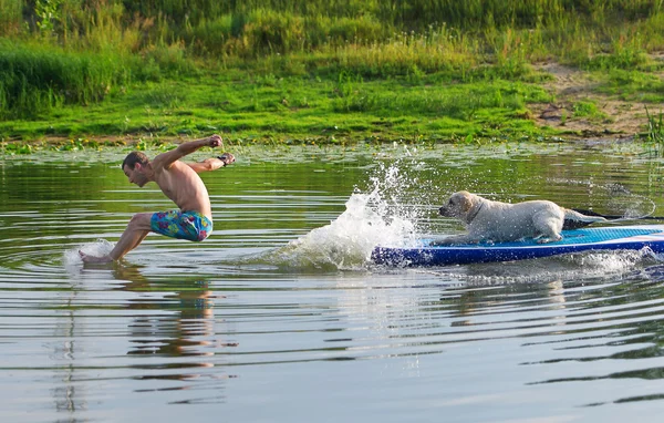 The young man and dog in the boat. The  jumps from the  in water. — Stock Photo, Image