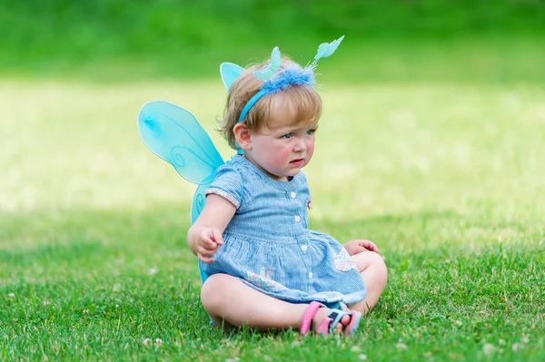 La pequeña hada en un vestido azul se sienta en el césped . —  Fotos de Stock