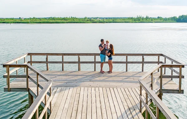 Glada unga kaukasiska familj med tre år gamla dotter stå på en flod pir. — Stockfoto