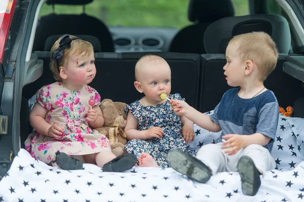 Bambini seduti nel bagagliaio dell'auto. Tre bambini mangiano caramelle . — Foto Stock