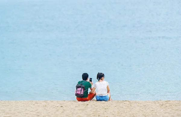 Paar mit Rucksack und Handy sitzt zusammen am Strand — Stockfoto