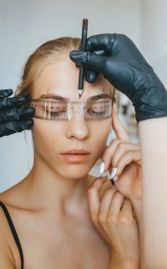 Usta, özel bir cetvelle işlemden önce müşterinin kaşlarının hatlarını kontrol eder. Kalıcı kaş makyaj prosedürü.