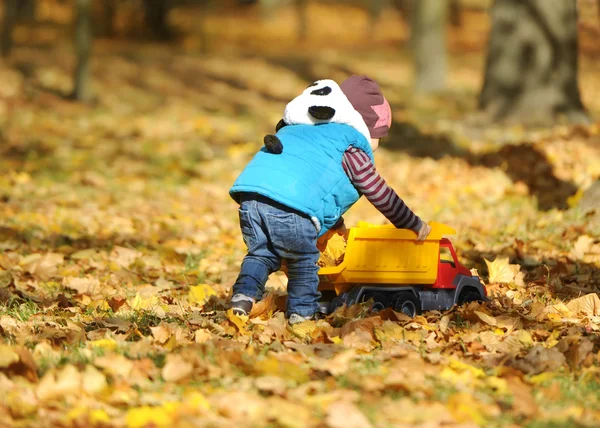 The kid plays with a toy machine in autumn park — Stock Photo, Image