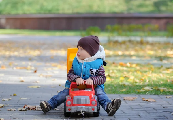 The kid plays with a toy machine in autumn park — Stock Photo, Image