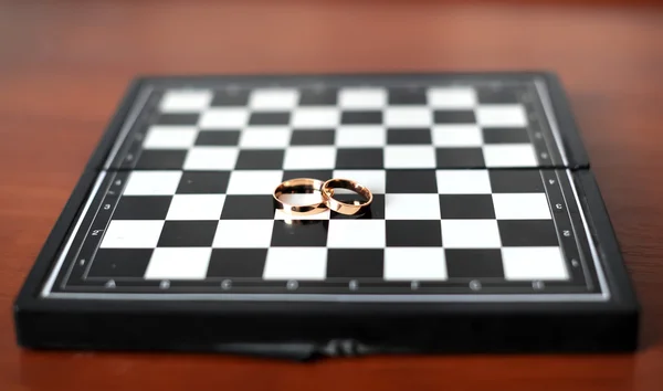 Anillos de boda se encuentran en un tablero de ajedrez —  Fotos de Stock