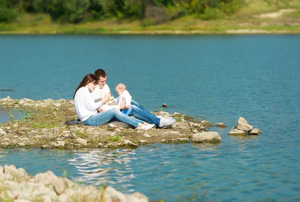 Het kleine meisje en haar ouders zitten aan de rivier. — Stockfoto