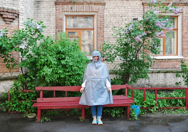 Fille en imperméable debout près d'un banc rouge — Photo