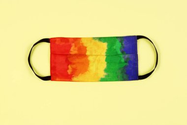 Sarı arka planda çok renkli koruyucu maske. Gökkuşağı renkleriyle bezenmiş tek kullanımlık tıbbi maske. Koronavirüse karşı koruma. Sağlık ve Tıp Konsepti