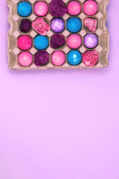 Huevos de Pascua y flores en caja de huevos sobre fondo rosa violeta, espacio de copia de vista superior, imagen vertical — Foto de Stock