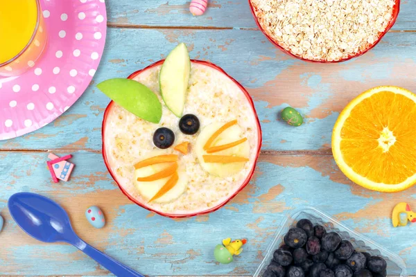 Pequeno-almoço criativo para crianças. farinha de aveia com frutas e suco de laranja. fundo de madeira azul, vista superior. Páscoa ideia café da manhã para crianças Imagens Royalty-Free