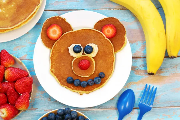 Kul idé för barn frukost. Björnformade pannkakor med bär på blått träbord, ovanifrån. Hälsosam mat för barn. Rolig mat för barn. Royaltyfria Stockfoton