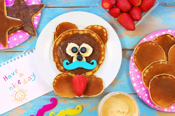 Divertida idea para el desayuno infantil. Panqueques en forma de oso con bayas y pasta de chocolate en la mesa de madera azul, vista superior. Comida saludable para niños. Comida divertida para niños. Imágenes De Stock Sin Royalties Gratis