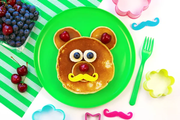 O idee amuzantă pentru micul dejun pentru copii. Clătite în formă de urs cu fructe de pădure pe placă verde, vedere de sus. Alimente sănătoase pentru copii. Mâncare amuzantă pentru copii . — Fotografie, imagine de stoc