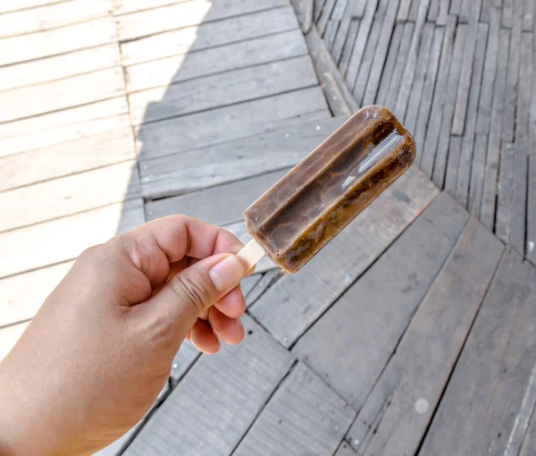 Icecream stick in hand and wooden background — Stock Photo, Image