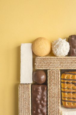 Sarı arka planda şekerler, kurabiyeler, gofretler ve şekerlemeler..