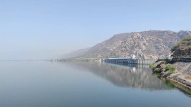 Gün ışığında mavi gökyüzü altında dağlık bir yerdeki baraj manzarasının görüntüsü.
